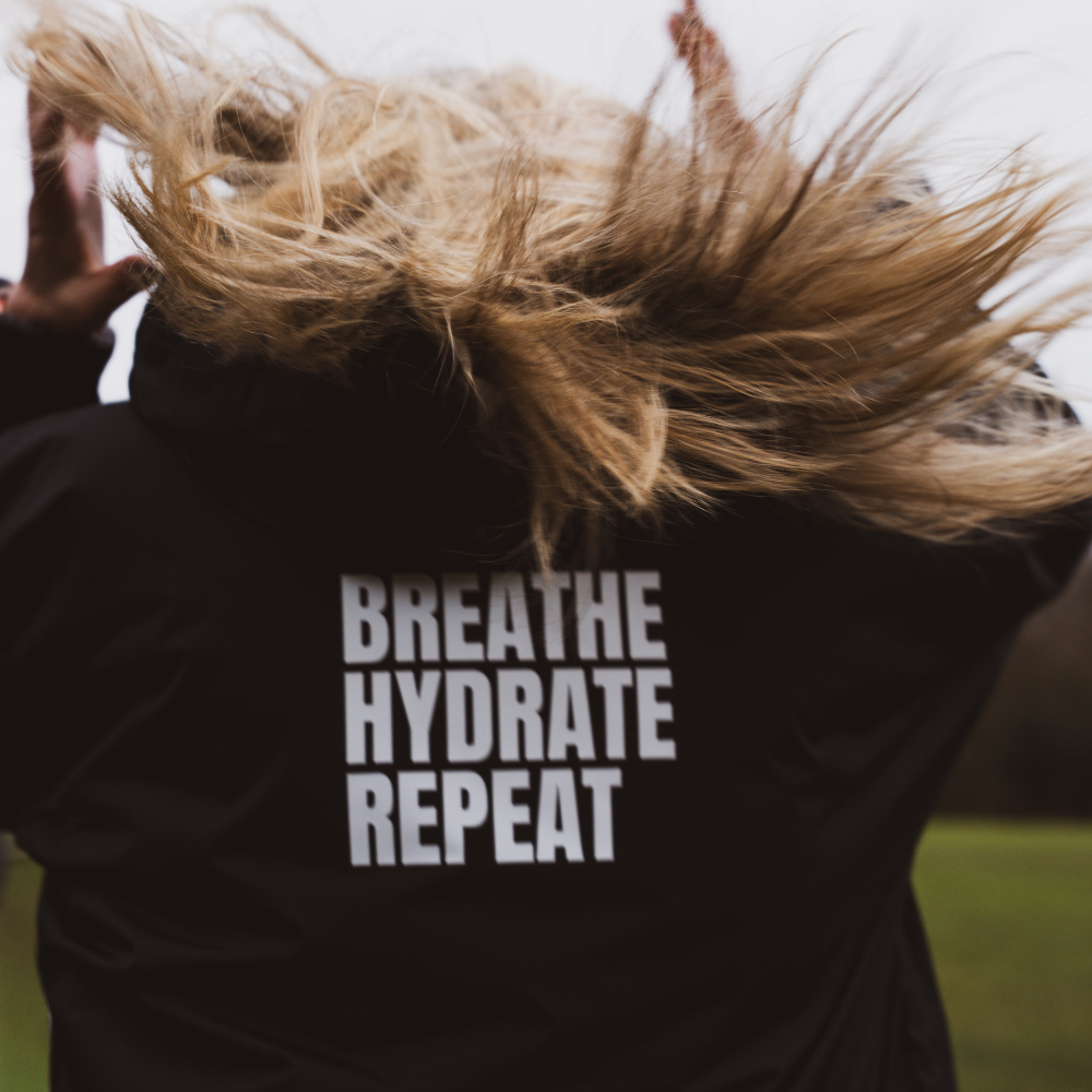 Person wearing a black coat with 'Breathe Hydrate Repeat' text outdoors.